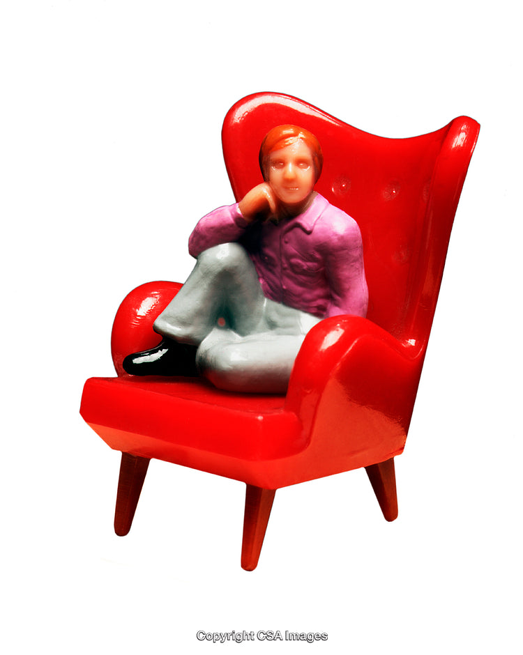 Miniature Figurine Relaxing in a Bright Red Armchair on White Background