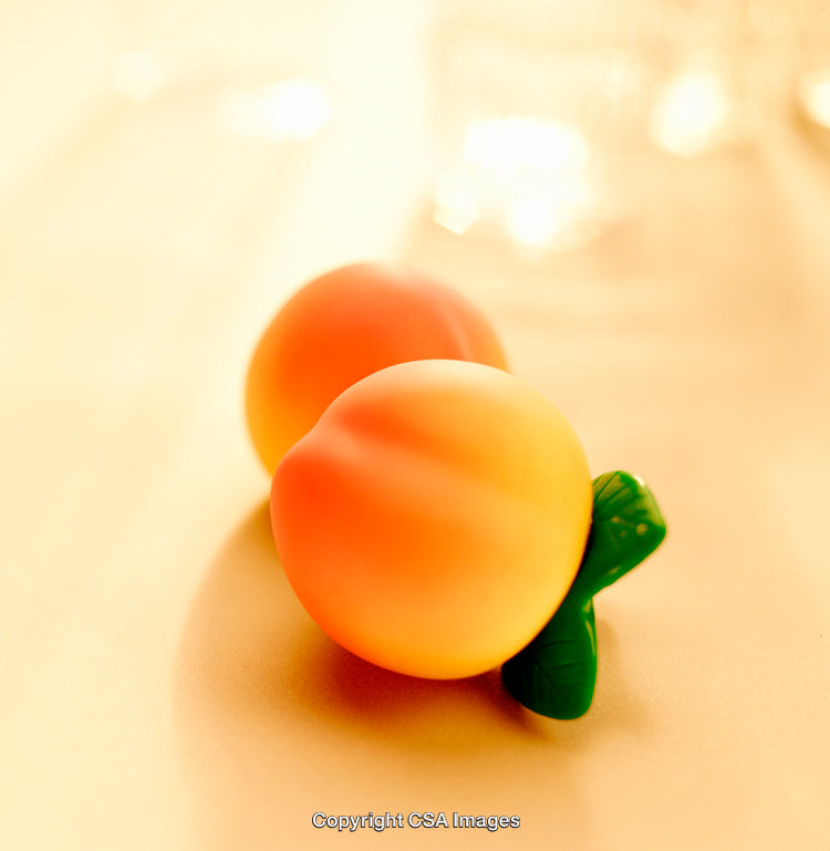 Pair of Plastic Peach-Shaped Toys with Soft Warm Background Lighting