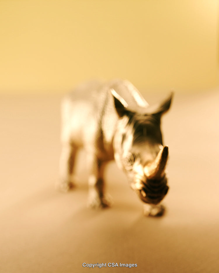 Blurred Golden Rhinoceros Toy Against a Gradient Yellow Background