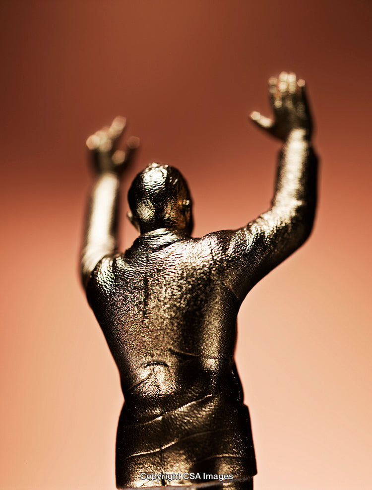 Golden Figurine Standing Against a Warm Light Background with Raised Arms