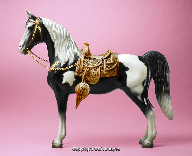 Black and White Toy Horse with Golden Saddle on Pink Background