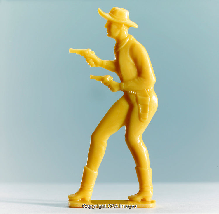 Yellow Plastic Cowboy Figure Holding Revolvers on a Light Blue Background