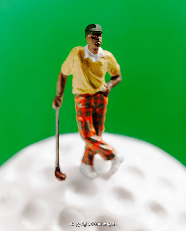 Miniature Golfer Figure Standing on a Golf Ball Against Green Background