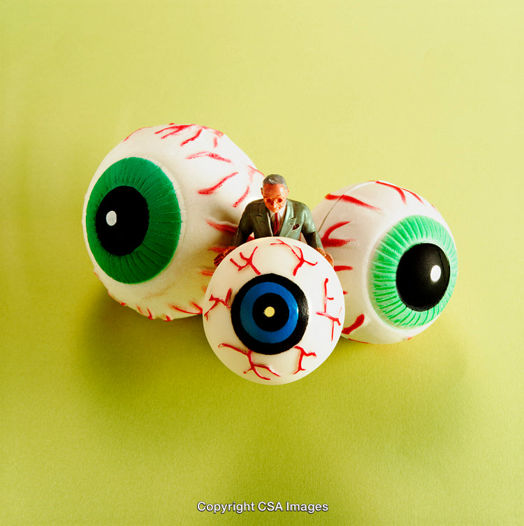 Miniature Figure Surrounded by Large Artificial Eyeballs on Green Surface