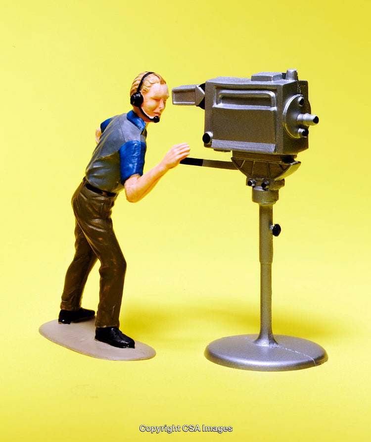 Toy Cameraman Figure Operating a Studio Camera Against Yellow Background