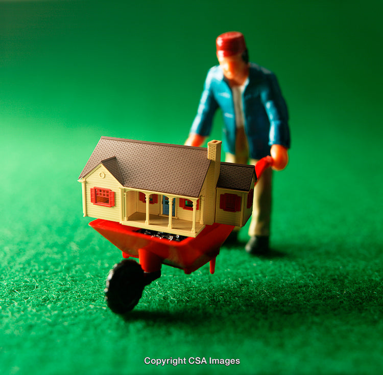 Toy Figurine With House on Wheelbarrow on Vibrant Green Surface