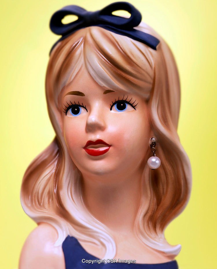 Close-Up of a Stylized Blonde Female Head Figurine with Yellow Backdrop