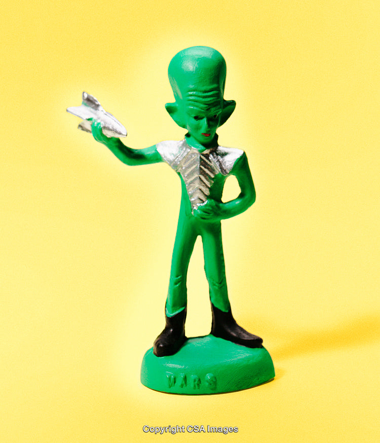 Green Alien Toy Figurine Holding Spaceship on Bright Yellow Background